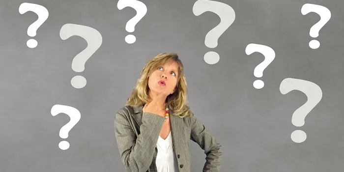 疑問を感じるジェスチャーをする女性と背景に沢山の？マーク